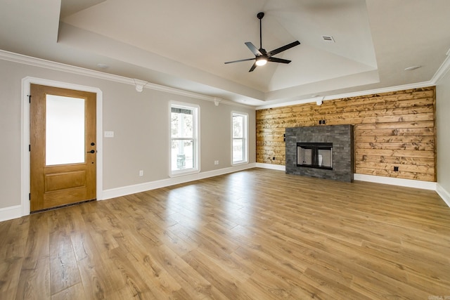 unfurnished living room featuring light wood finished floors, a stone fireplace, a ceiling fan, a tray ceiling, and visible vents