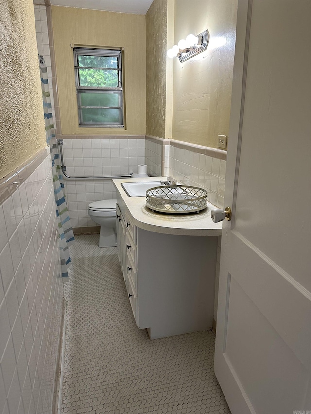 bathroom with toilet, tile walls, wainscoting, and vanity