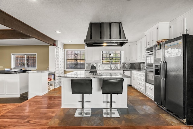 7510 Briarwood Dr, Little Rock, AR 72205 - kitchen featuring black fridge, light stone countertops, wall chimney exhaust hood, and white cabinetry