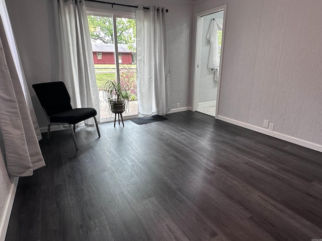 sitting room featuring baseboards, a textured wall, and dark wood-style floors