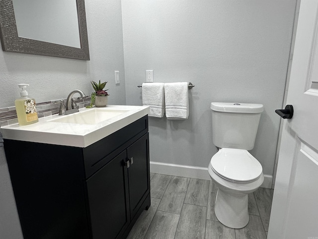 half bathroom with vanity, baseboards, wood finished floors, and toilet