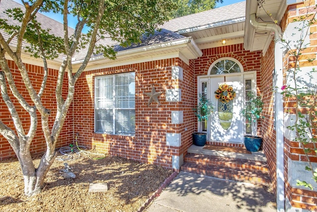 view of exterior entry featuring brick siding and a shingled roof