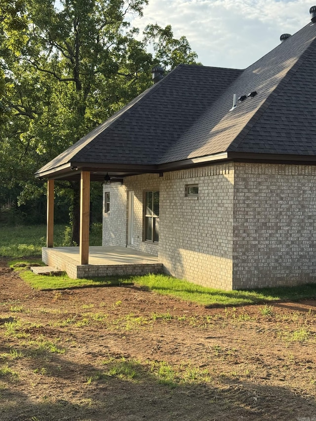 rear view of house with brick siding, a shingled roof, and a patio area