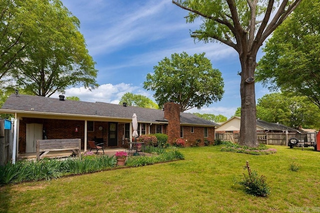back of property with fence, a patio, a chimney, brick siding, and a yard