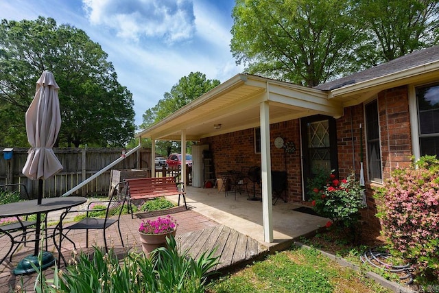 view of patio with a deck, fence, and outdoor dining space