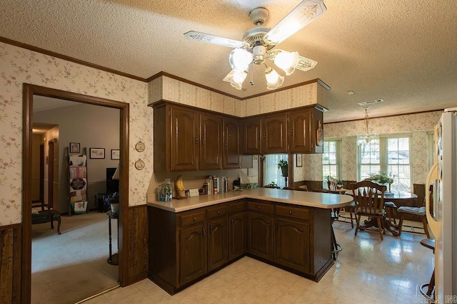 kitchen with crown molding, light countertops, a textured ceiling, ceiling fan with notable chandelier, and wallpapered walls