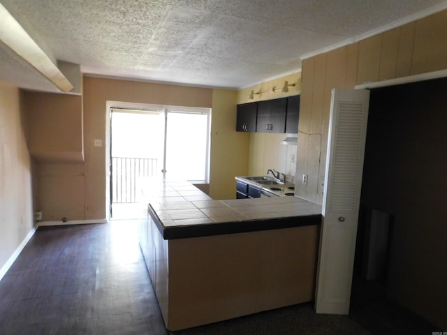 kitchen with a peninsula, baseboards, dark wood-type flooring, tile countertops, and a sink