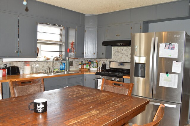 kitchen featuring appliances with stainless steel finishes, a sink, wooden counters, backsplash, and under cabinet range hood