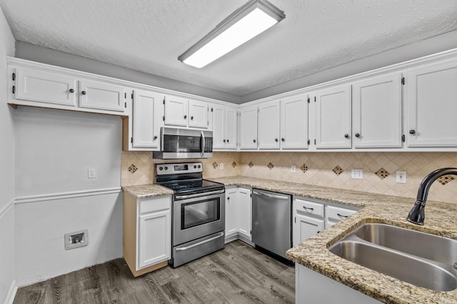 kitchen featuring white cabinets, a sink, stainless steel appliances, wood finished floors, and tasteful backsplash