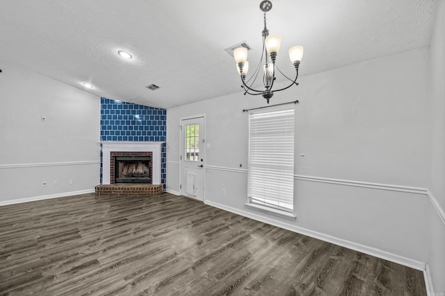 unfurnished living room with wood finished floors, a fireplace, a textured ceiling, a notable chandelier, and vaulted ceiling
