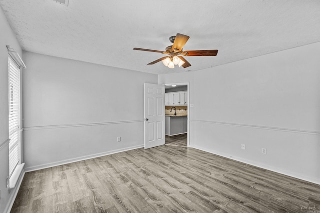 unfurnished bedroom with baseboards, a sink, a ceiling fan, and wood finished floors