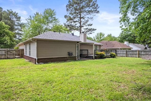 back of property with a chimney, a lawn, a wooden deck, a fenced backyard, and a shingled roof