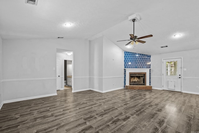 unfurnished living room featuring ceiling fan, visible vents, a fireplace, vaulted ceiling, and dark wood-style floors