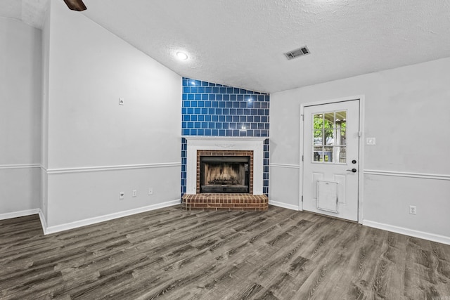 unfurnished living room featuring a brick fireplace, a textured ceiling, wood finished floors, lofted ceiling, and visible vents