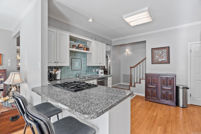 kitchen featuring crown molding, a sink, dishwasher, a breakfast bar area, and white cabinetry