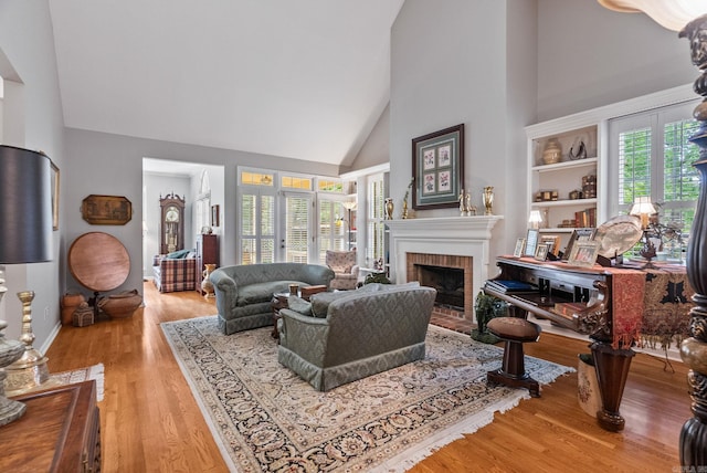 living room with high vaulted ceiling, baseboards, a brick fireplace, and light wood-style flooring