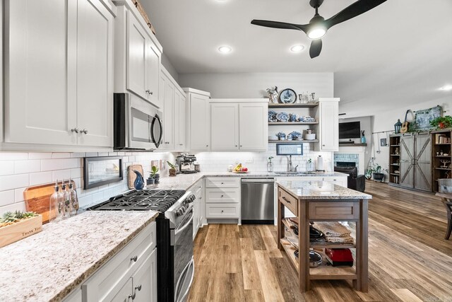 kitchen with open shelves, a sink, stainless steel appliances, a ceiling fan, and decorative backsplash
