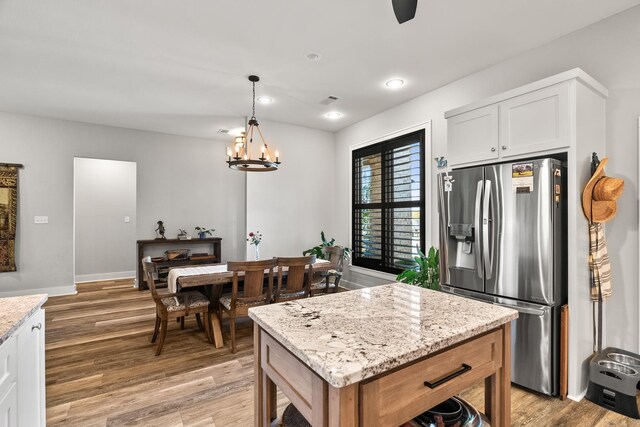 kitchen with light stone countertops, light wood-style floors, white cabinetry, stainless steel fridge with ice dispenser, and a notable chandelier