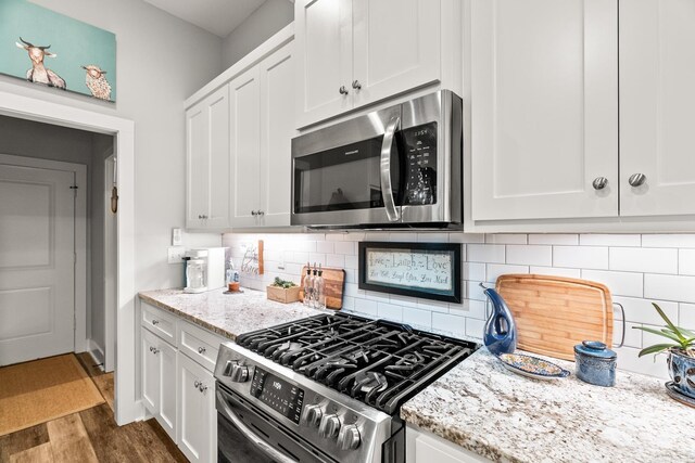 kitchen featuring decorative backsplash, white cabinets, stainless steel appliances, and wood finished floors