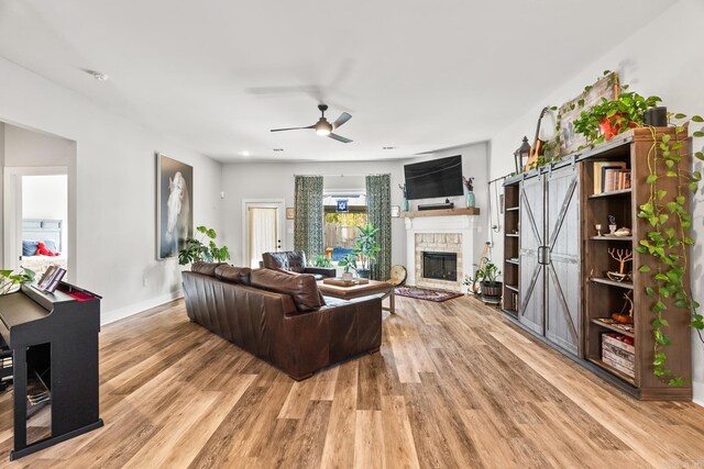 living room with a ceiling fan, baseboards, light wood finished floors, and a fireplace