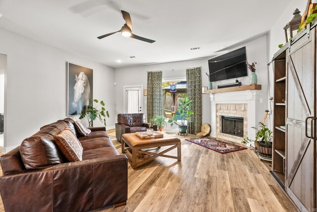 living room with ceiling fan, a brick fireplace, wood finished floors, and visible vents