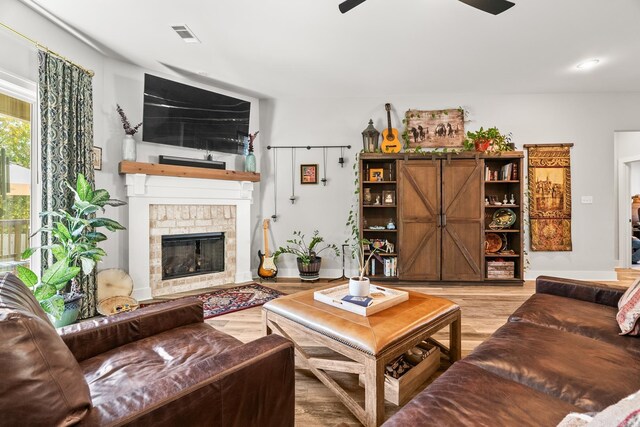 living area featuring light wood-style floors, ceiling fan, and a fireplace