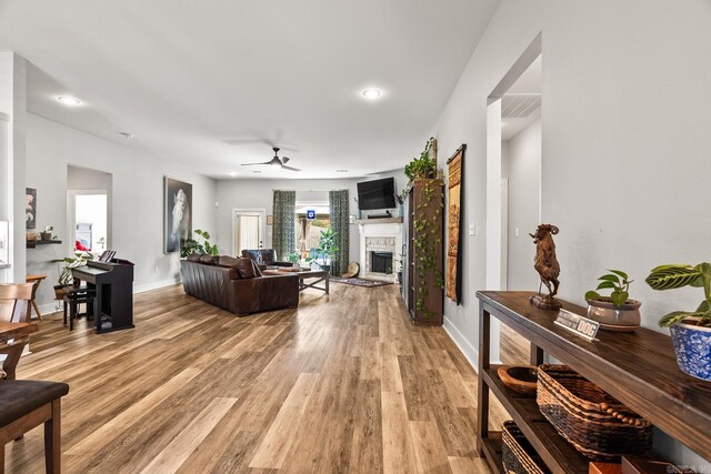 living area with baseboards, a fireplace with raised hearth, a ceiling fan, and light wood finished floors