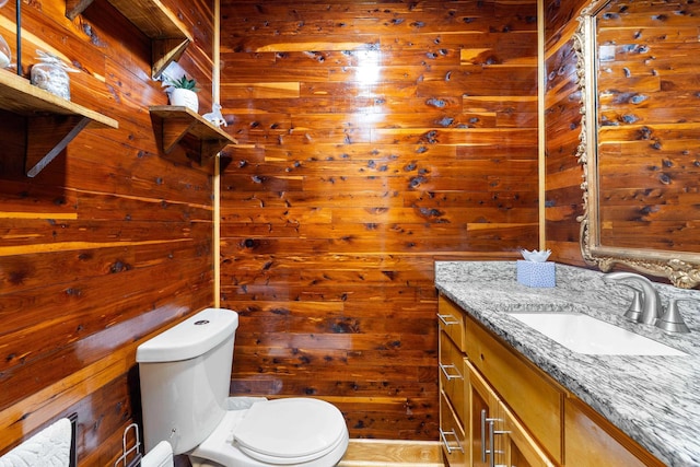 bathroom with toilet, wood walls, and vanity