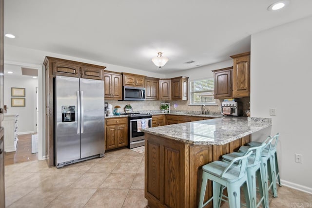 kitchen featuring decorative backsplash, a peninsula, a kitchen bar, light stone counters, and stainless steel appliances