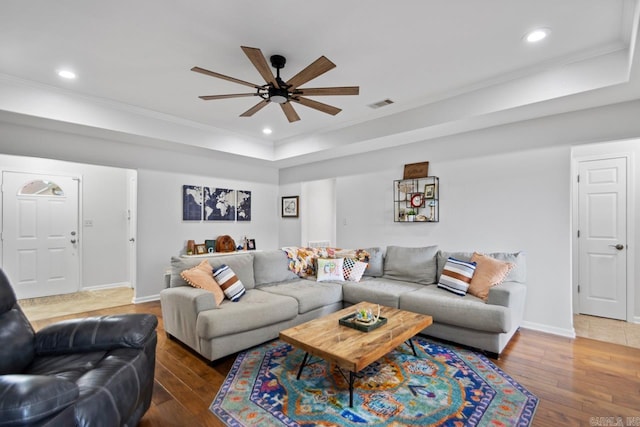 living room with ceiling fan, a raised ceiling, visible vents, ornamental molding, and hardwood / wood-style flooring