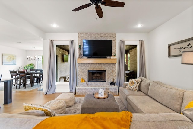 living area featuring a fireplace, ceiling fan with notable chandelier, recessed lighting, and wood finished floors