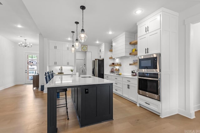 kitchen with light countertops, tasteful backsplash, a sink, light wood-style flooring, and appliances with stainless steel finishes