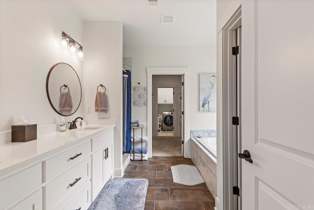 full bath featuring washer / clothes dryer, visible vents, tiled tub, and vanity