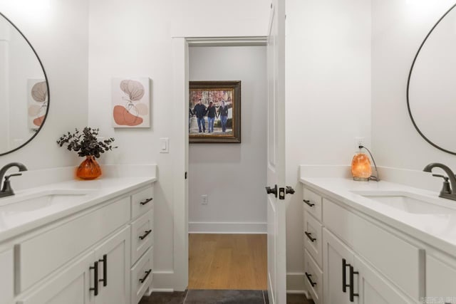 bathroom featuring baseboards, two vanities, a sink, and wood finished floors