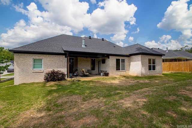 rear view of house with a lawn, brick siding, fence, a patio, and a shingled roof