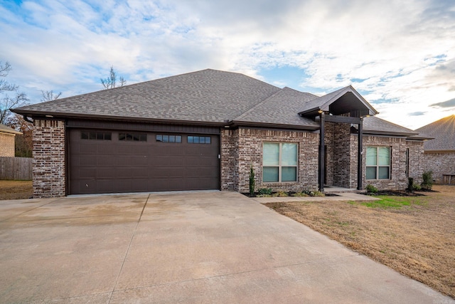 ranch-style house featuring concrete driveway, brick siding, an attached garage, and roof with shingles