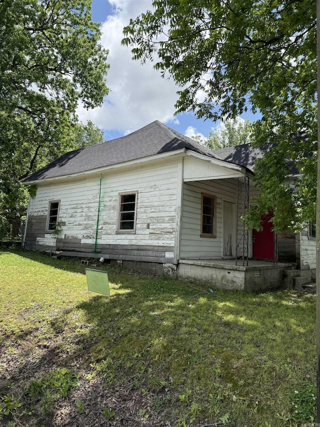 view of side of home featuring a shingled roof, a yard, and a porch