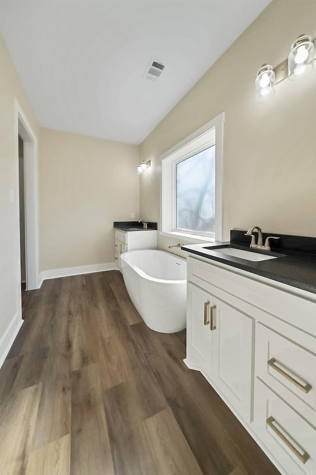 bathroom with visible vents, a freestanding bath, wood finished floors, and vanity