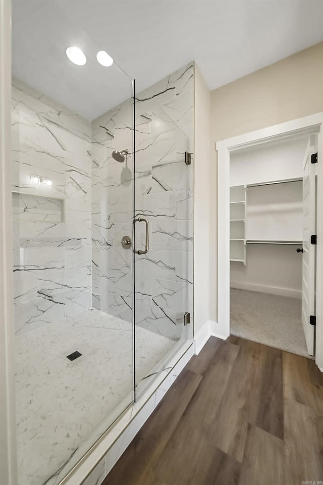 full bathroom featuring a walk in closet, wood finished floors, baseboards, a marble finish shower, and recessed lighting