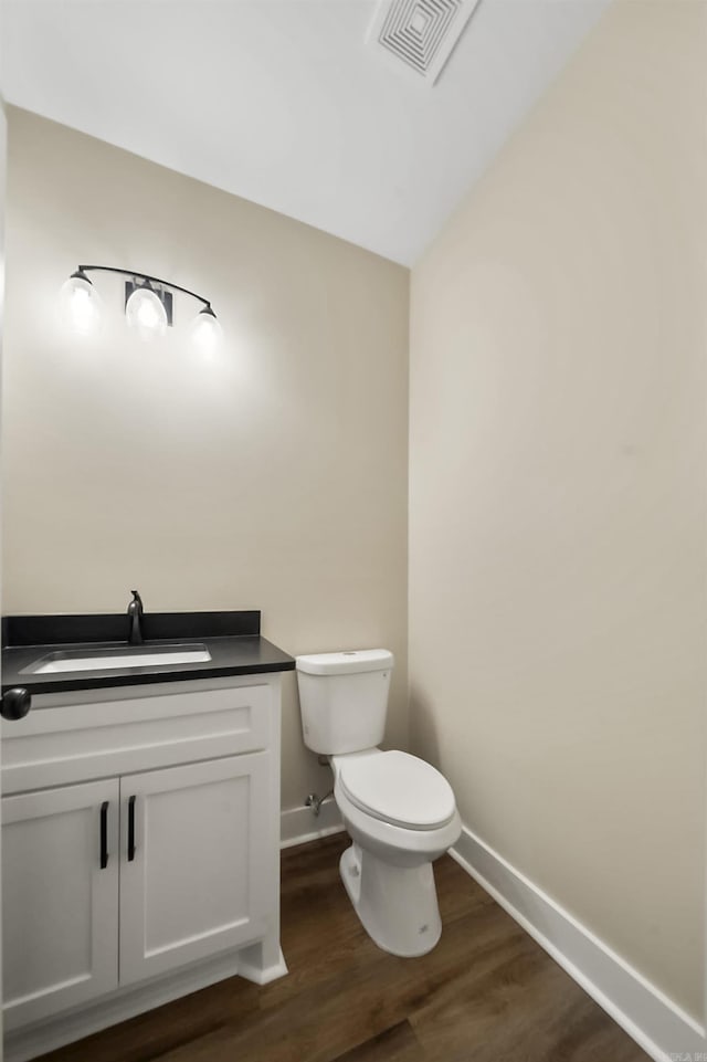 half bathroom with visible vents, baseboards, wood finished floors, and toilet