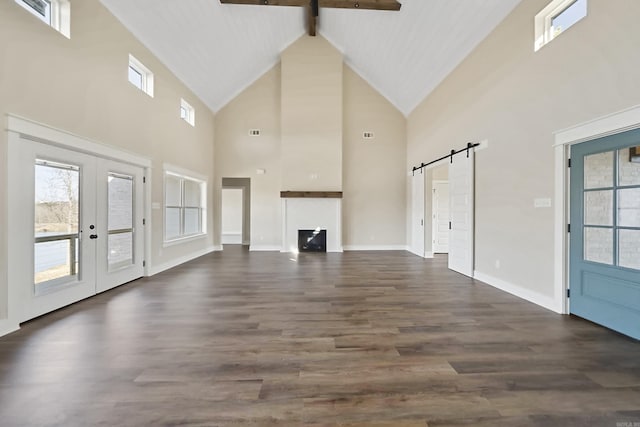 unfurnished living room featuring high vaulted ceiling, a barn door, a wealth of natural light, and dark wood-type flooring