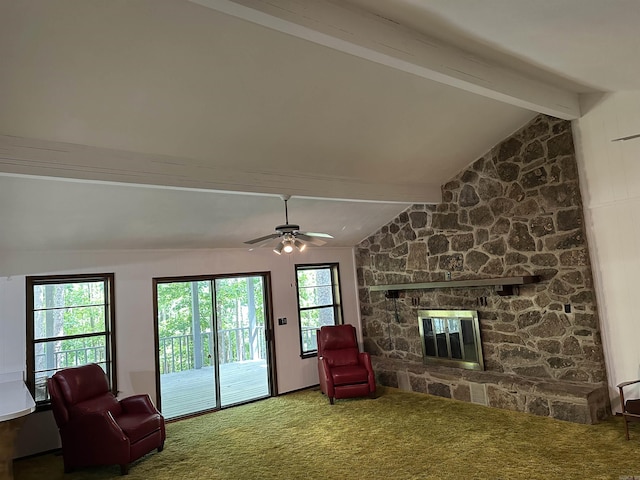 carpeted living area featuring a ceiling fan, a stone fireplace, plenty of natural light, and vaulted ceiling with beams
