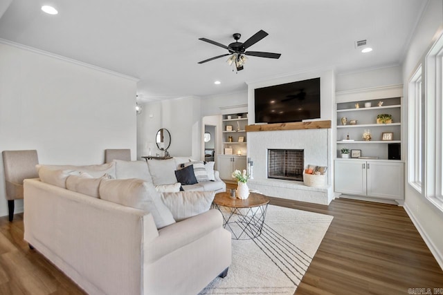 living area with crown molding, a fireplace with raised hearth, and wood finished floors