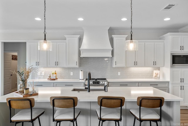 kitchen with pendant lighting, light countertops, white cabinetry, stainless steel microwave, and custom range hood