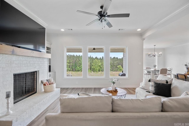living area with visible vents, a brick fireplace, ceiling fan with notable chandelier, ornamental molding, and recessed lighting