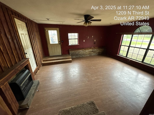 unfurnished living room with ceiling fan, a healthy amount of sunlight, attic access, and wood finished floors