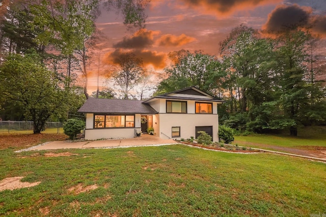 back of house at dusk featuring fence, an attached garage, a lawn, and stucco siding