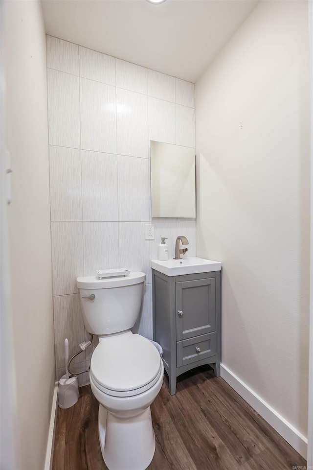 half bathroom with toilet, tile walls, wood finished floors, and vanity