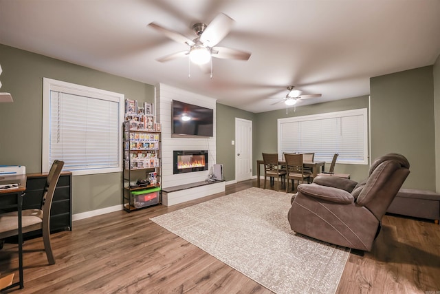 living room featuring a large fireplace, ceiling fan, baseboards, and wood finished floors