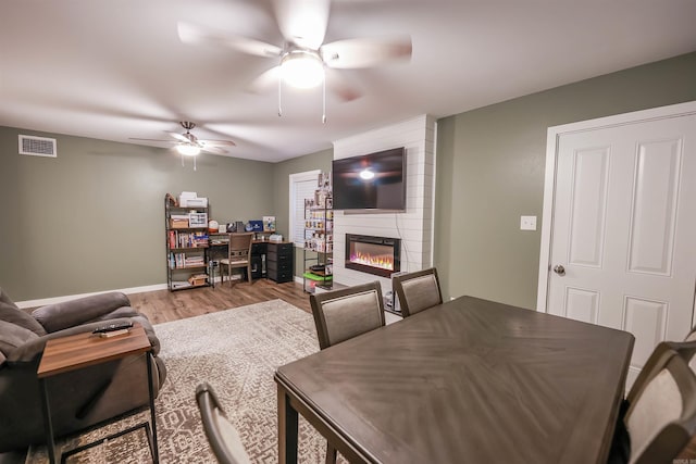living area with visible vents, wood finished floors, baseboards, a large fireplace, and a ceiling fan